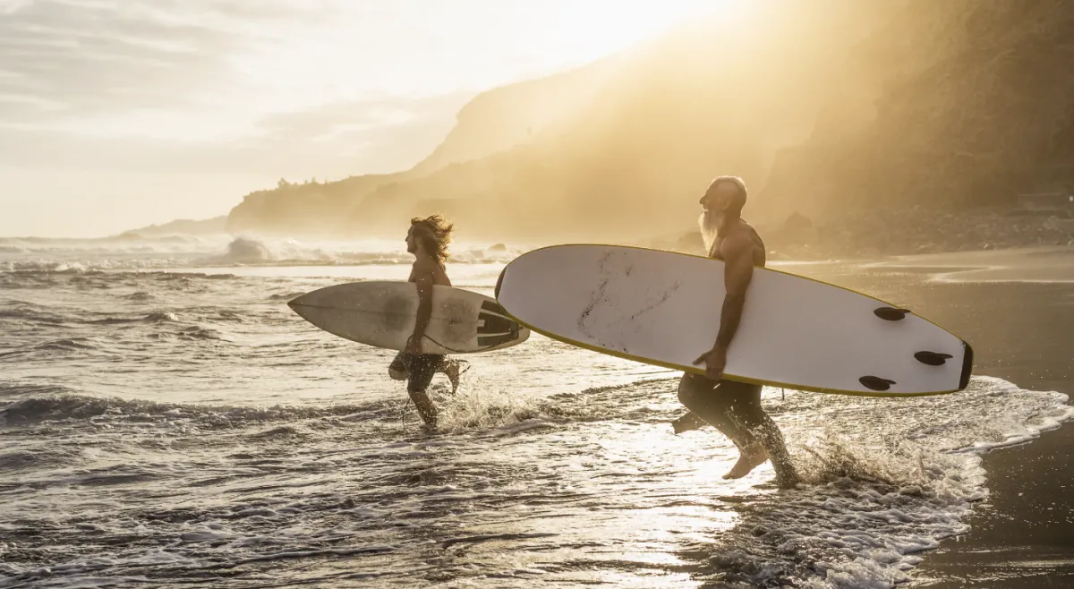 Two surfers walking into the water at sunset