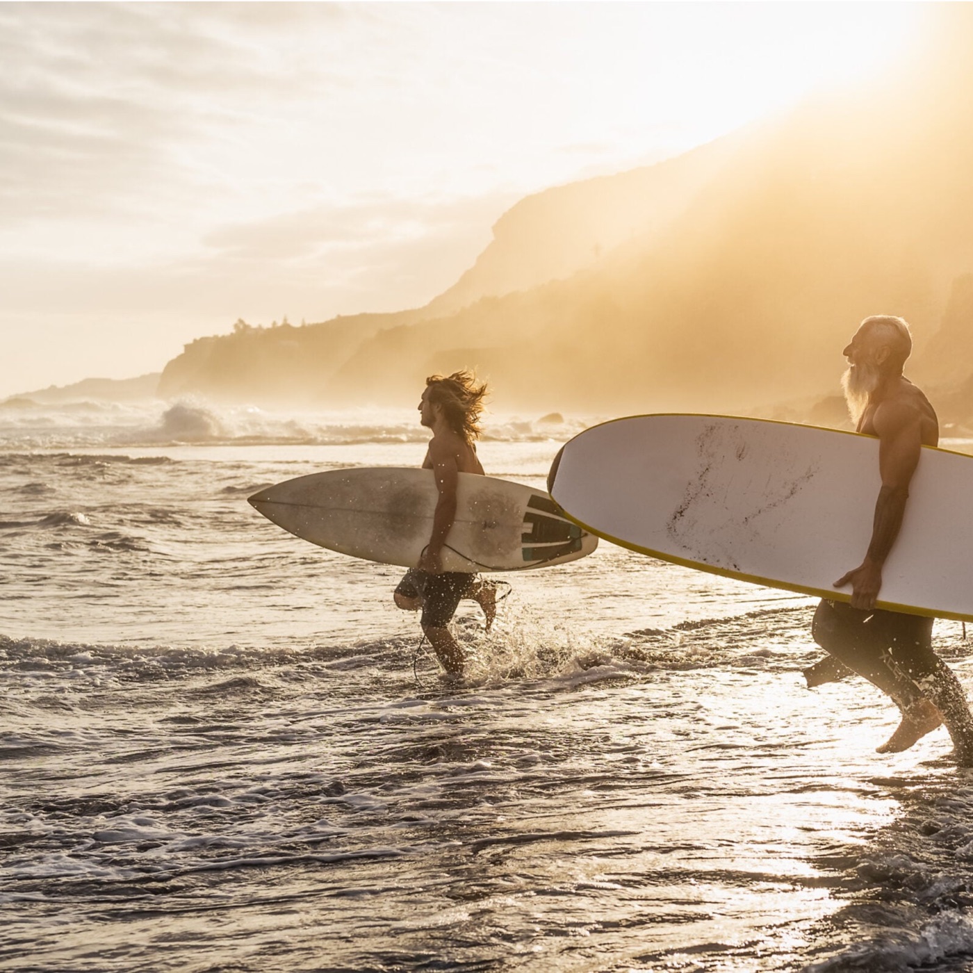 Two surfers walking into the water at sunset